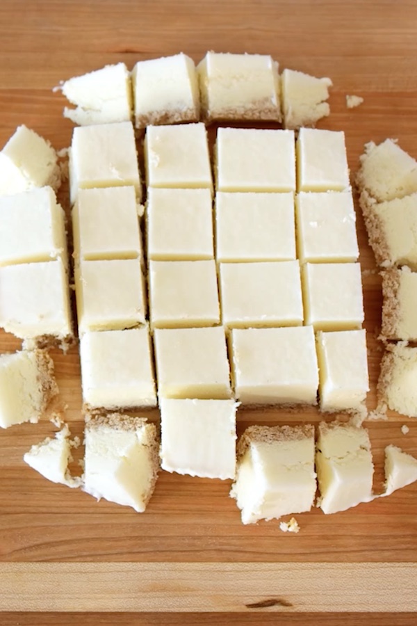 Frozen cheesecake is cut into many 1-inch pieces  on a wooden cutting board