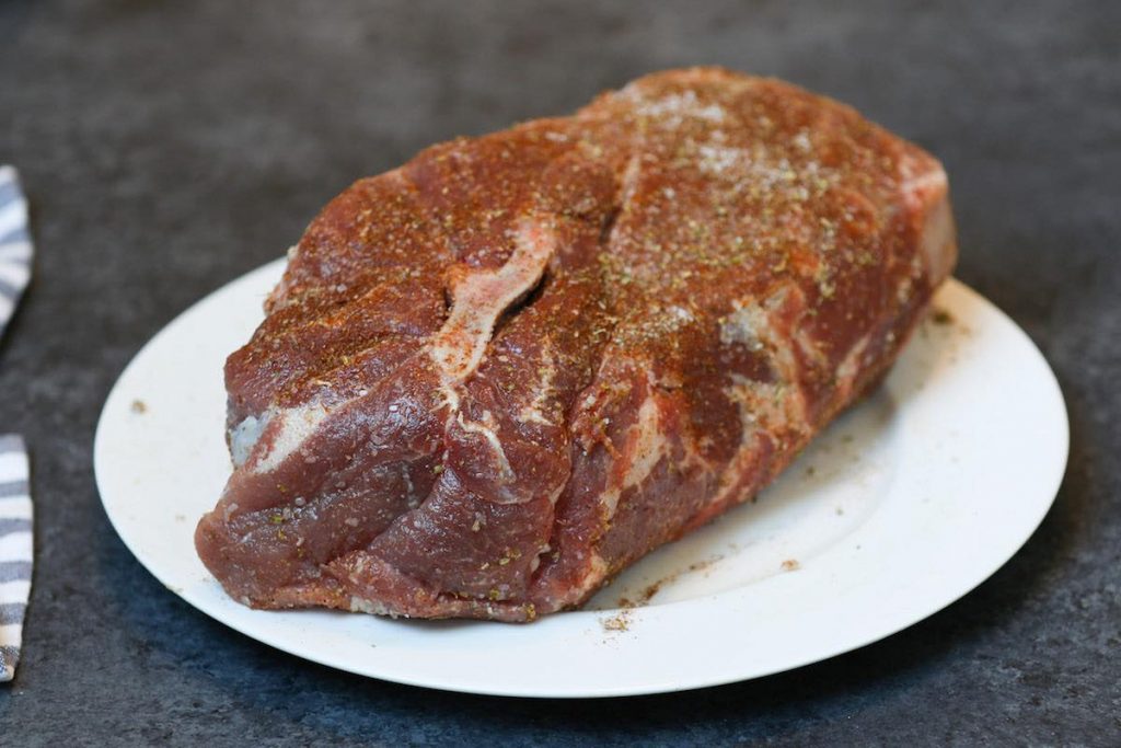 Seasoned raw pork shoulder on a white plate.