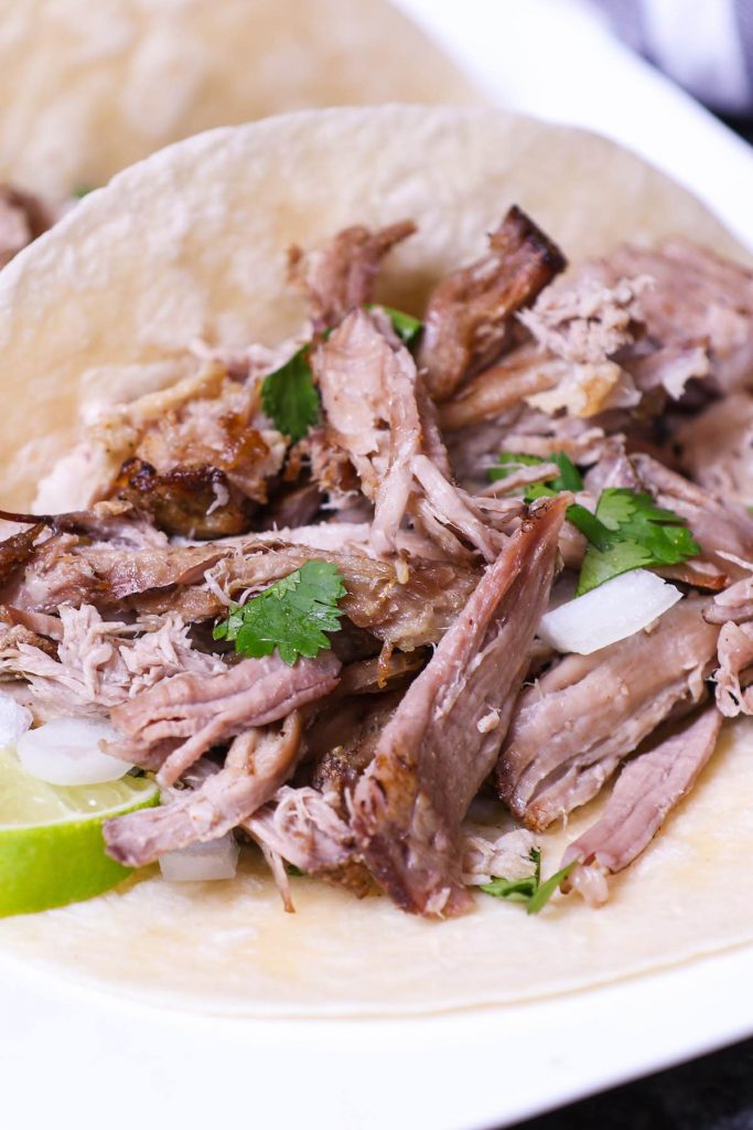 Shredded carnitas served on flour tortillas and topped with chopped onions and cilantro.