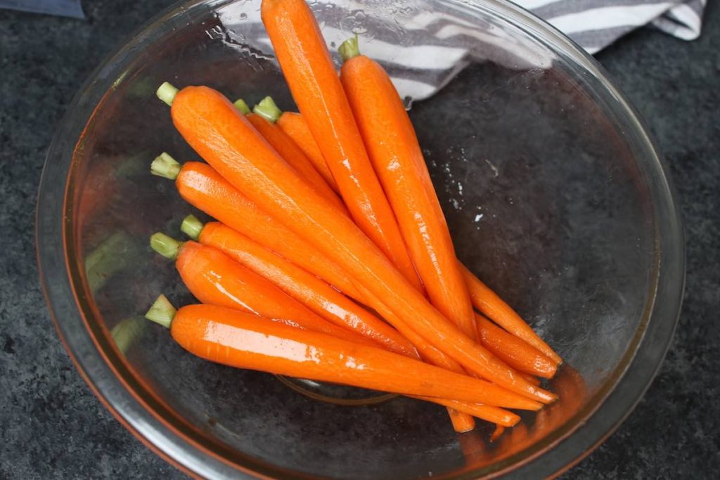 Zanahorias peladas sazonadas con miel y sal en un tazón transparente para mezclar.
