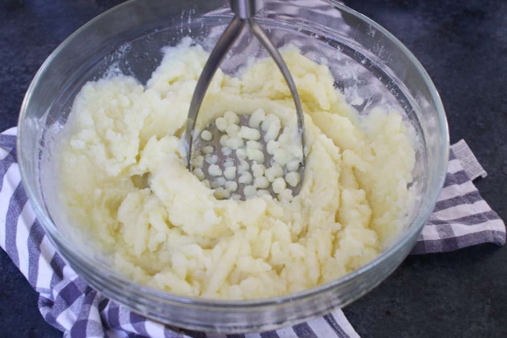 Mashing the cooked potatoes using a potato masher.