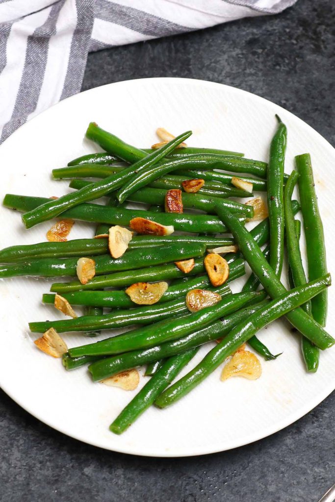 Sous vide green beans with garlic and oil served on a white plate.