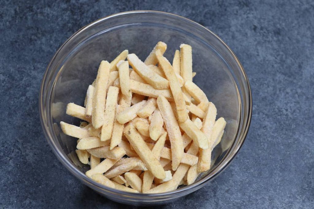 Season frozen french fries with salt and pepper in a large bowl.