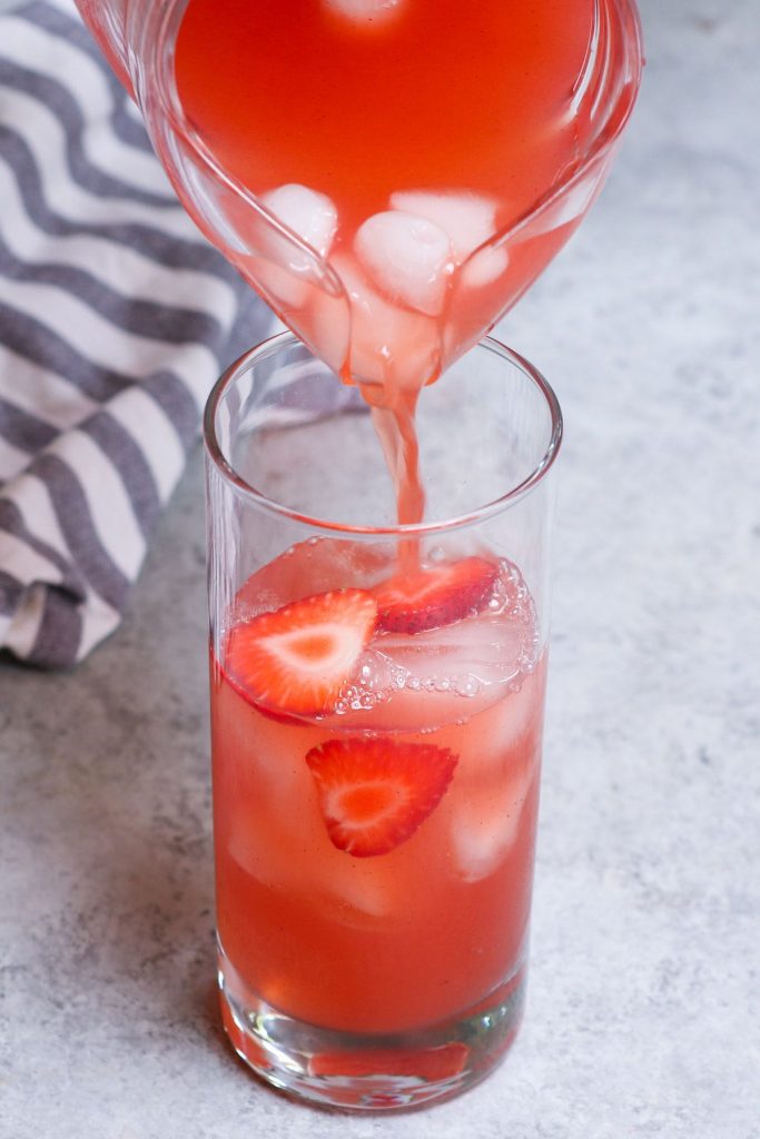 Pouring strawberry acai refresher into a high ball glass.