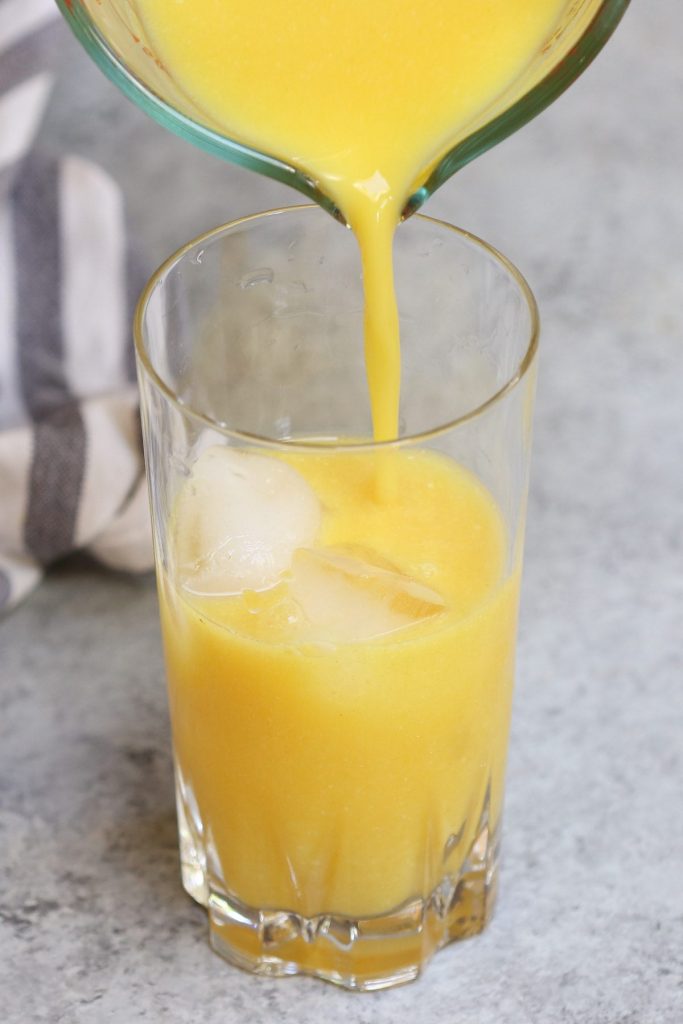 Closeup of pouring golden ginger drink into a tall glass.