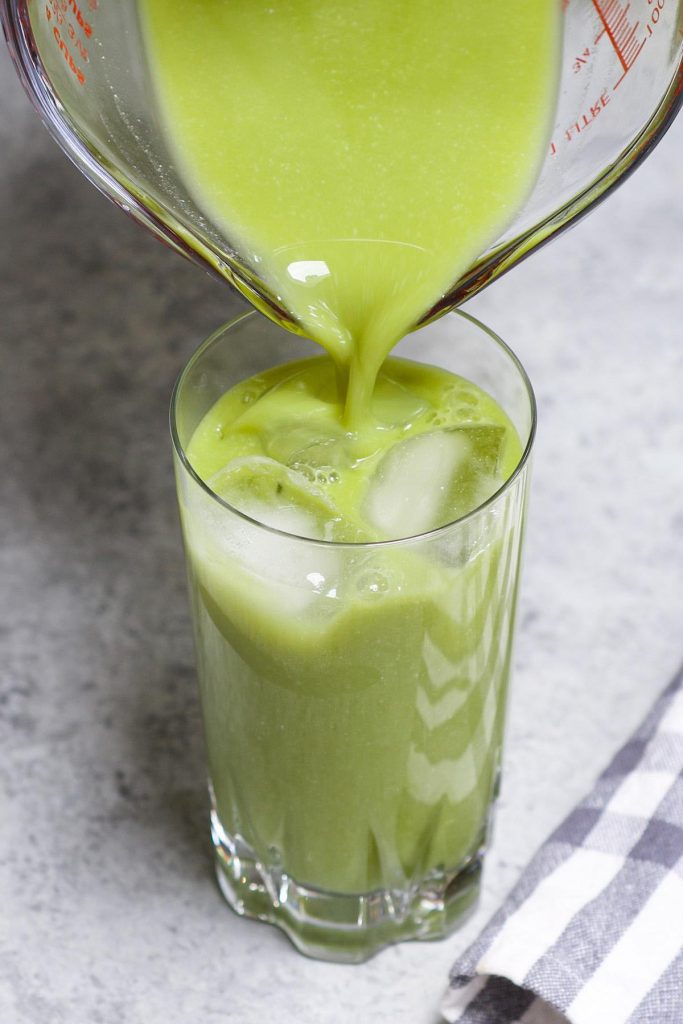 Pouring pineapple matcha drink mixture into a tall glass.