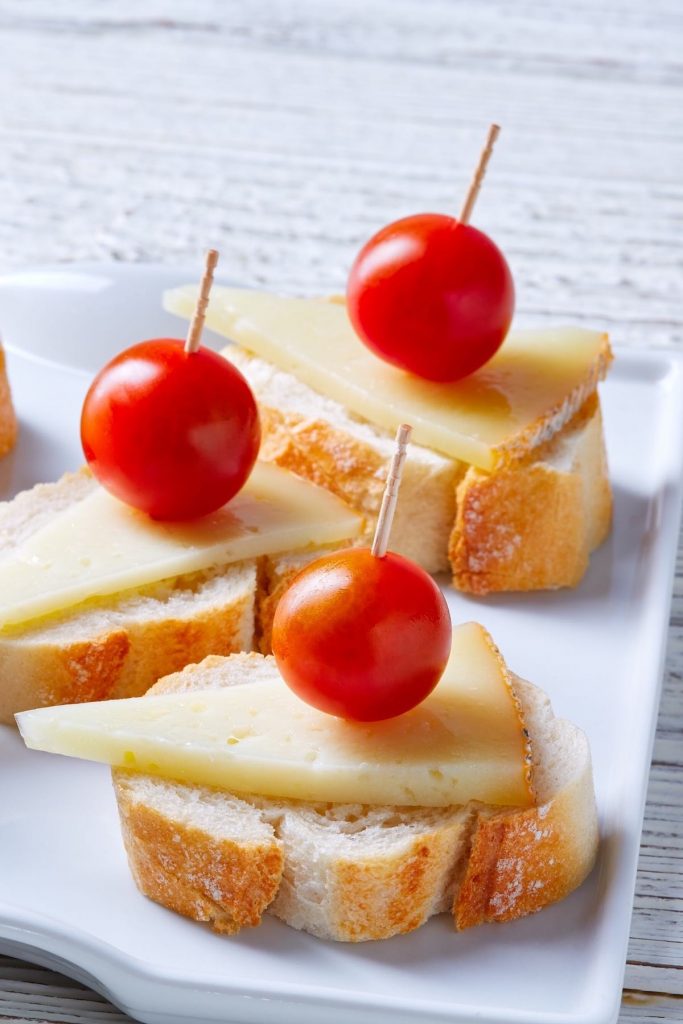 This Queso Manchego Crostini is an easy and delicious appetizer made with simple ingredients that pack in some big flavors! All you need is sliced bread, olive oil, Spanish Queso Manchego, and other favorite toppings to make a party platter or delightful finger food. #QuesoManchego #ManchegoCheese #Crostini