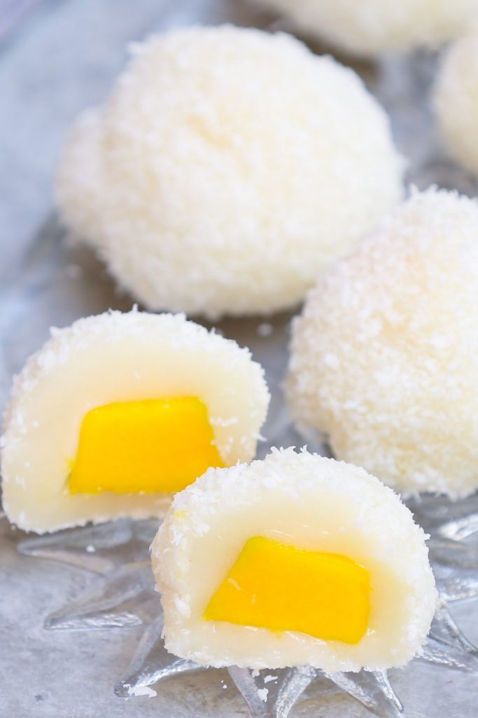 May I impress you with this refreshing homemade Japanese Mango Mochi? Tangy and sweet mango filling is covered with soft and chewy mochi cake. It’s rolled into mango mochi balls with a delicious shredded coconut coating, perfect for a hot summer day! This recipe is quick to make, and can be easily customized for vegan or dairy-free preferences. #MangoMochi
