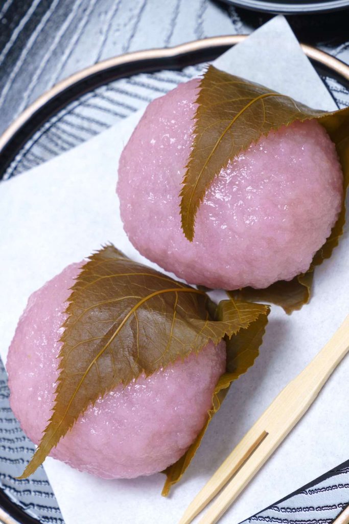 Easy Sakura Mochi with chewy and sticky rice cake on the outside, and sweet red bean paste filling on the inside! It’s rolled into beautiful pink mochi balls and covered with an edible pickled cherry blossom leaf. This Japanese dessert recipe is quick to make at home and perfect for celebrating the spring season or other special occasions. #SakuraMochi #PinkMochi