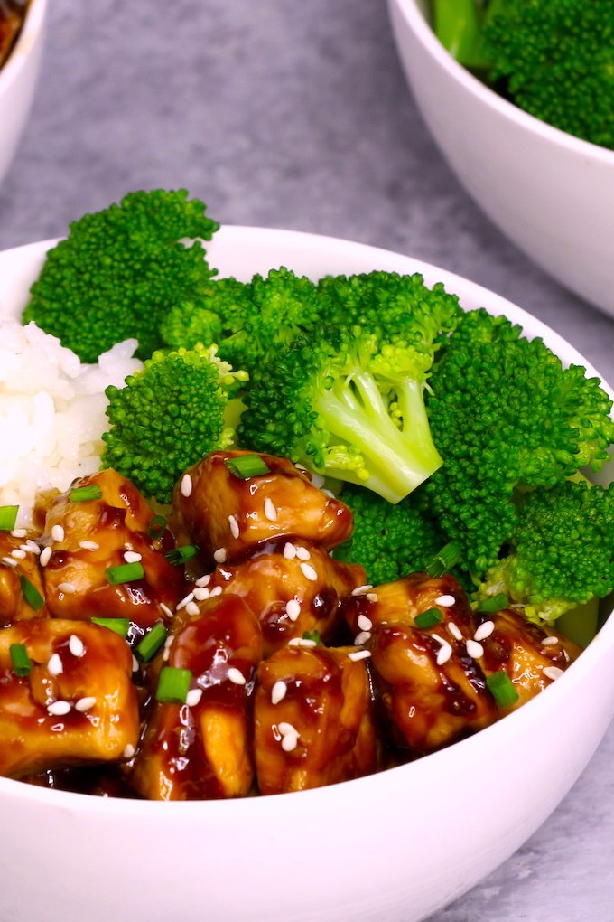 teriyaki chicken served on top of rice with steamed broccoli in a white bowl