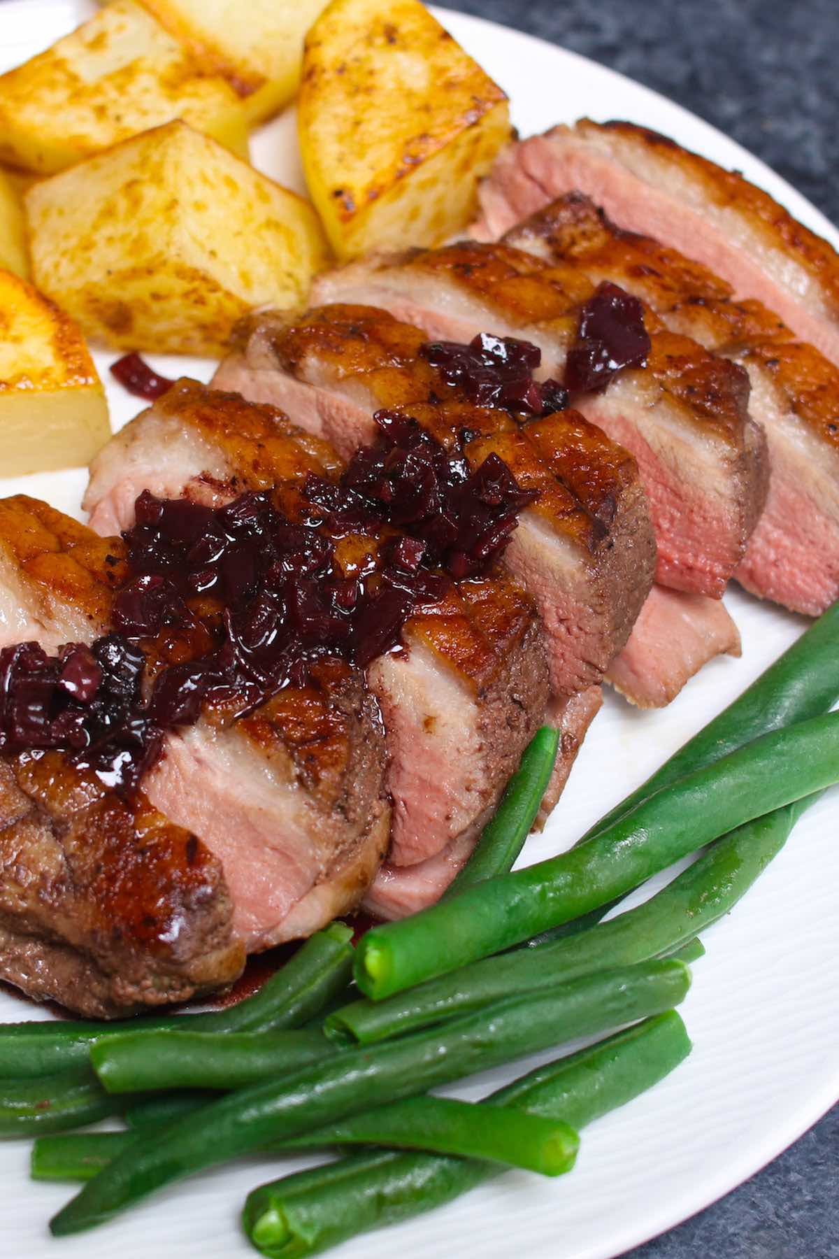 Sliced Sous Vide Duck Breast served with potatoes and green beans on a white plate.