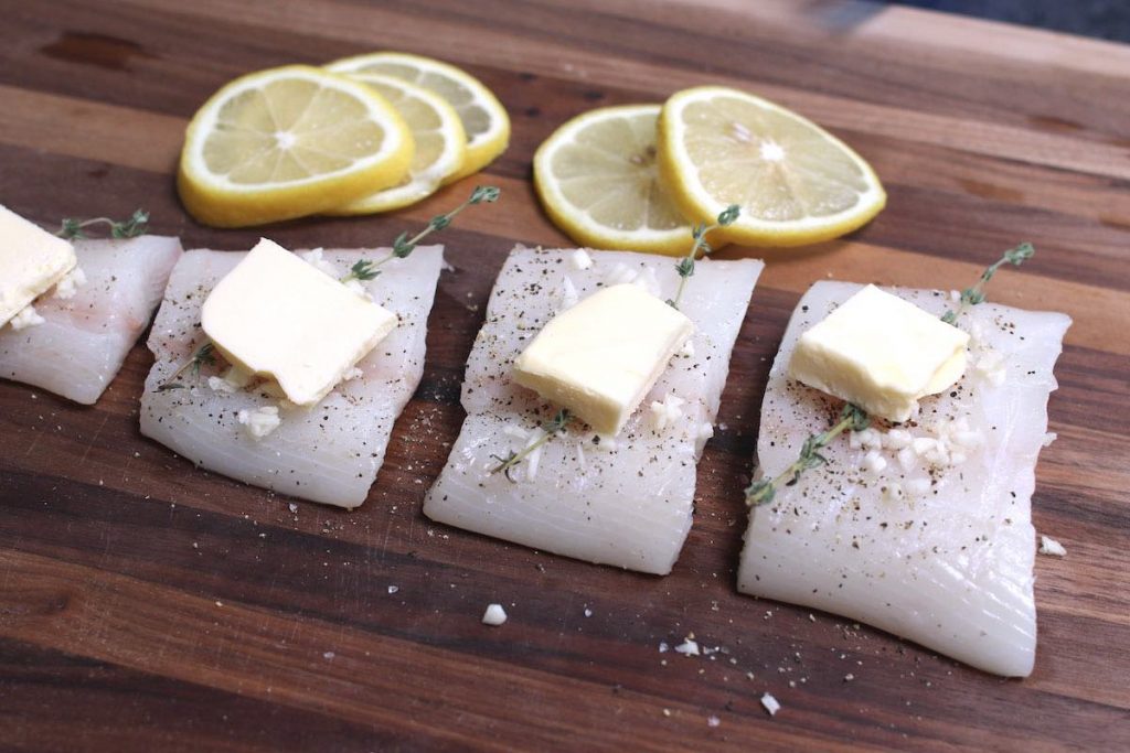 Raw halibut filets with seasoning and butter on top.