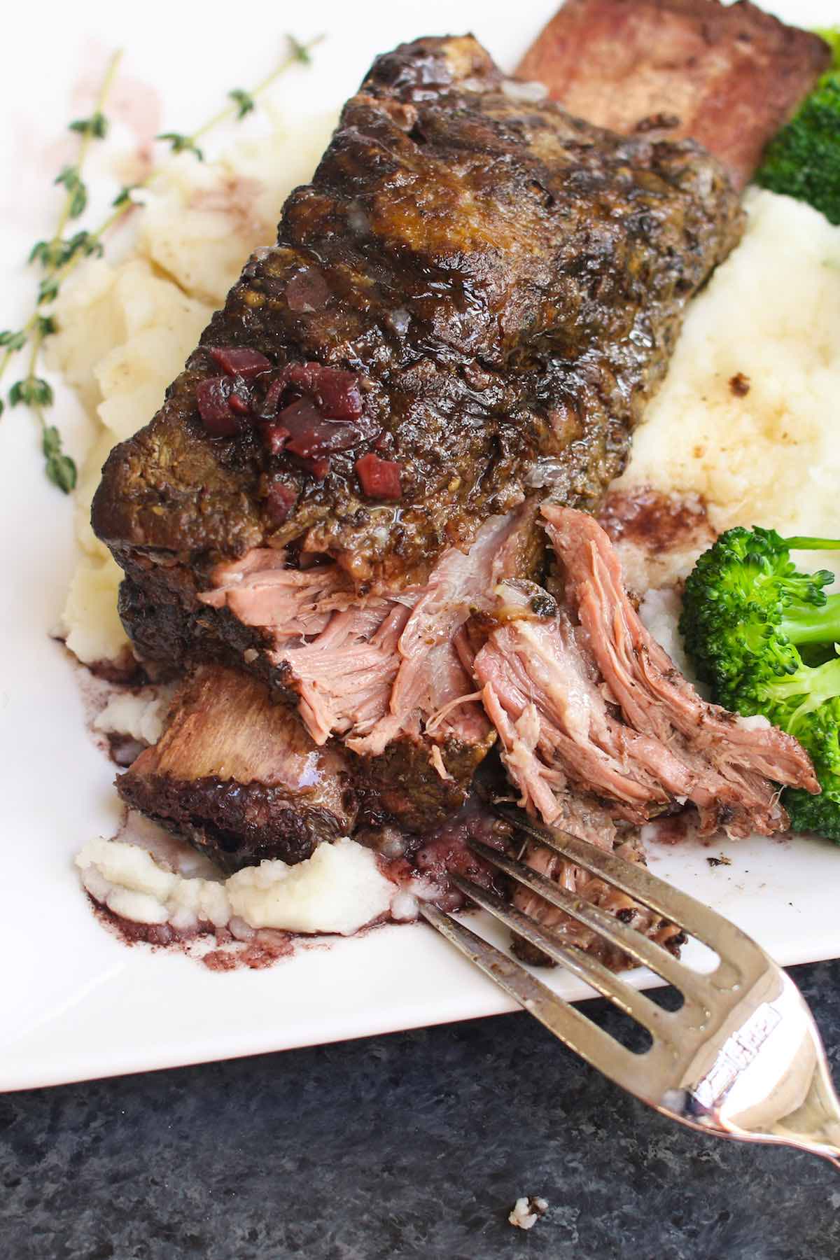 Close up showing the fall-off-the-bone tender flesh of Sous Vide Beef Short Ribs with red wine sauce, served on top of mashed potatoes with steamed broccoli.