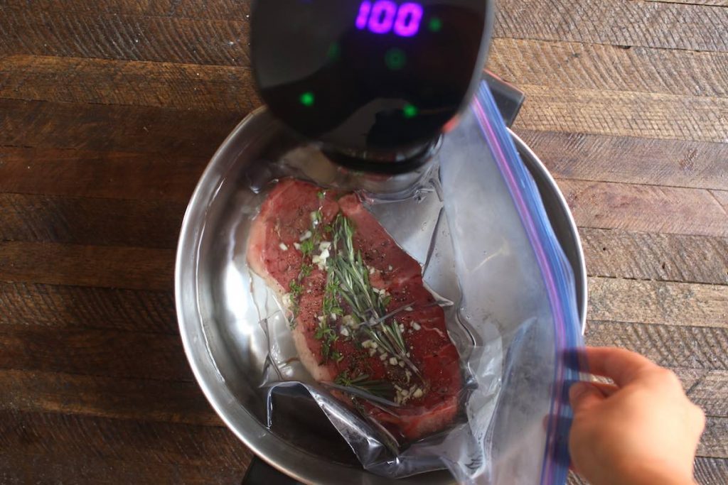 Photo of placing a sealed zip-lock bag with seasoned steak in the water bath.