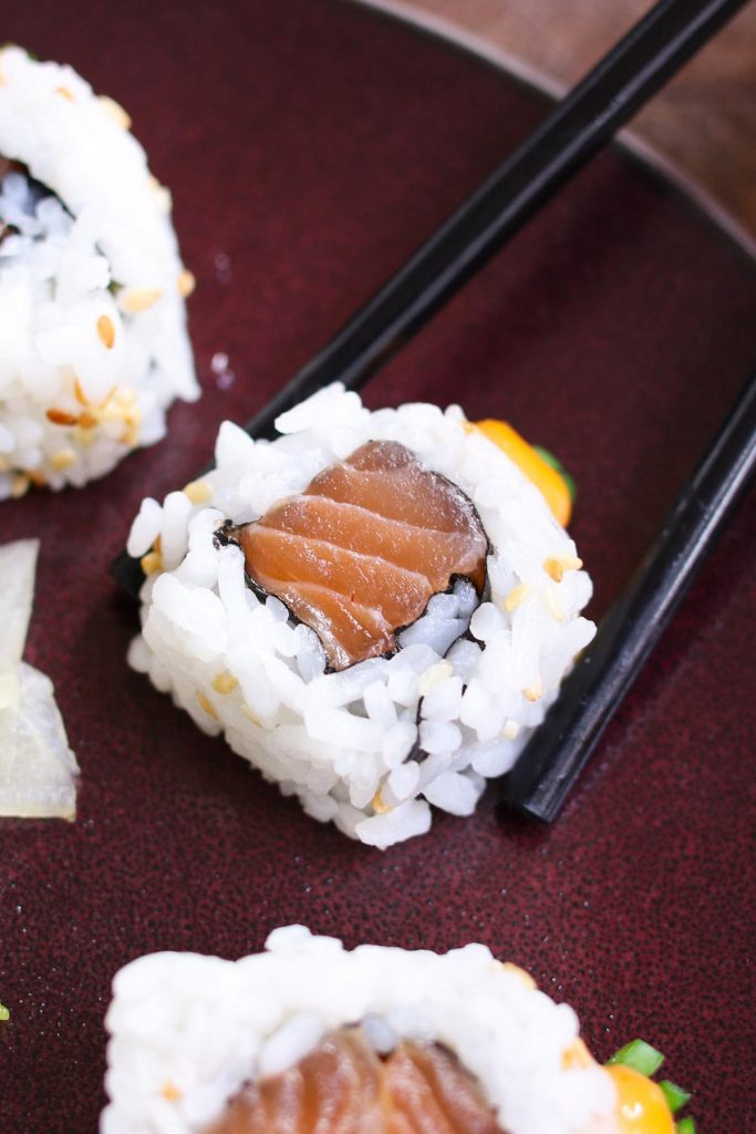 Photo showing using chopsticks picking a piece of spicy salmon roll.