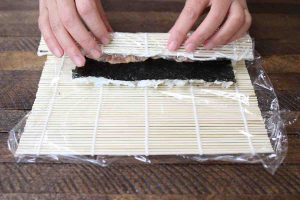 Place the thumbs underneath the bamboo mat and lift the edge up and over the filling.