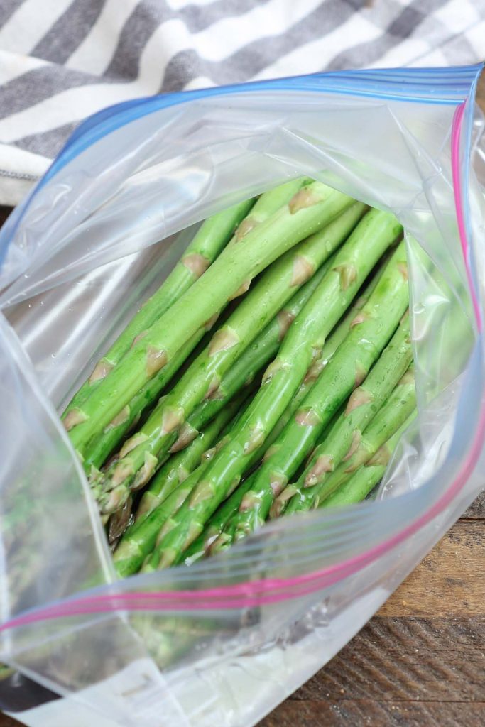 Drizzling olive oil over asparagus in a zip-lock bag.