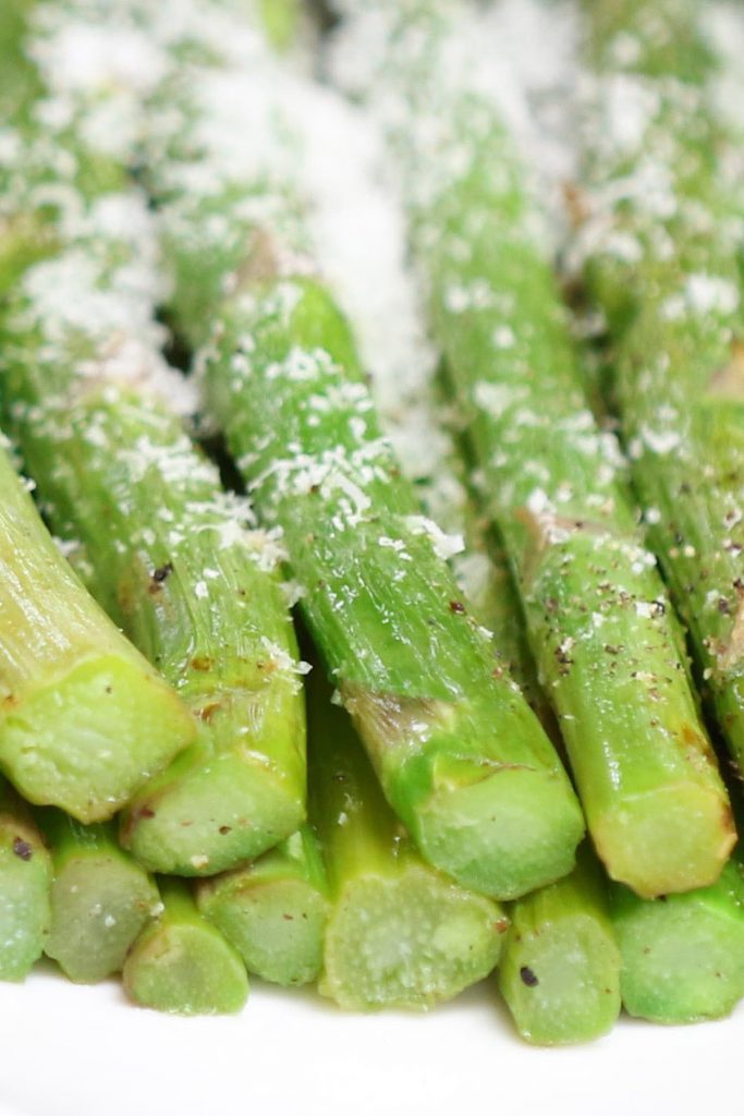 Closeup of the tender asparagus sprinkled with parmesan cheese on a white plate.