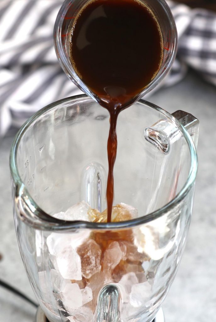 Pouring the chilled coffee over ice in a blender.