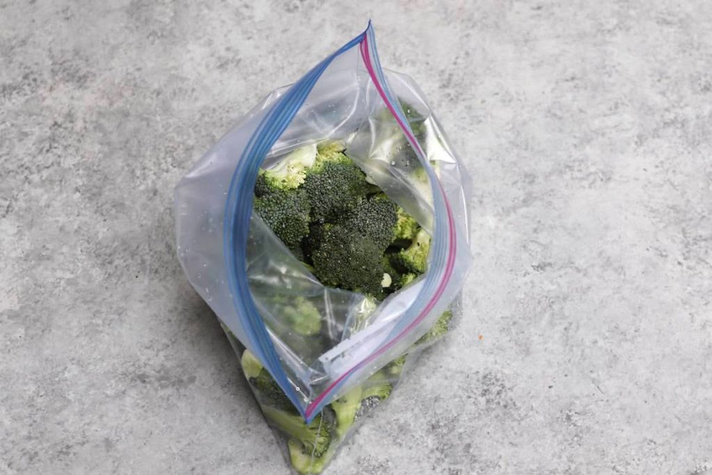 Adding broccoli florets and seasoning into a bag.