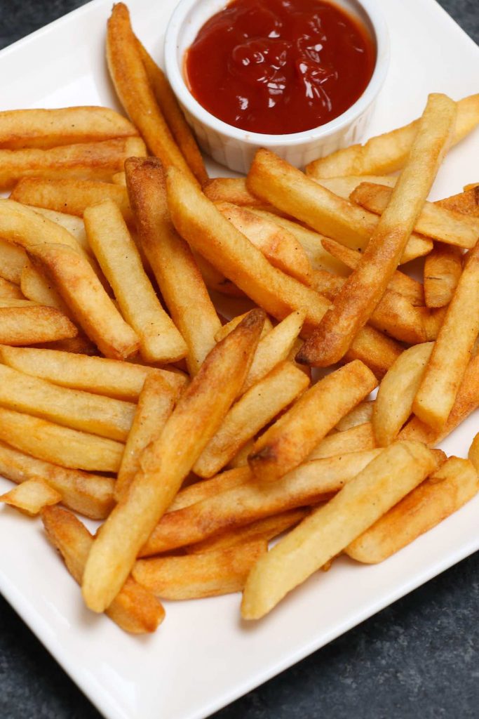Cooked French fries served with ketchup on a white plate.