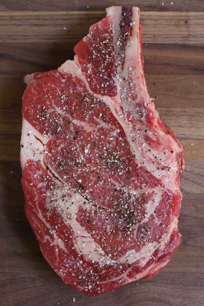 Ribeye steak seasoned with salt and pepper on a cutting board.
