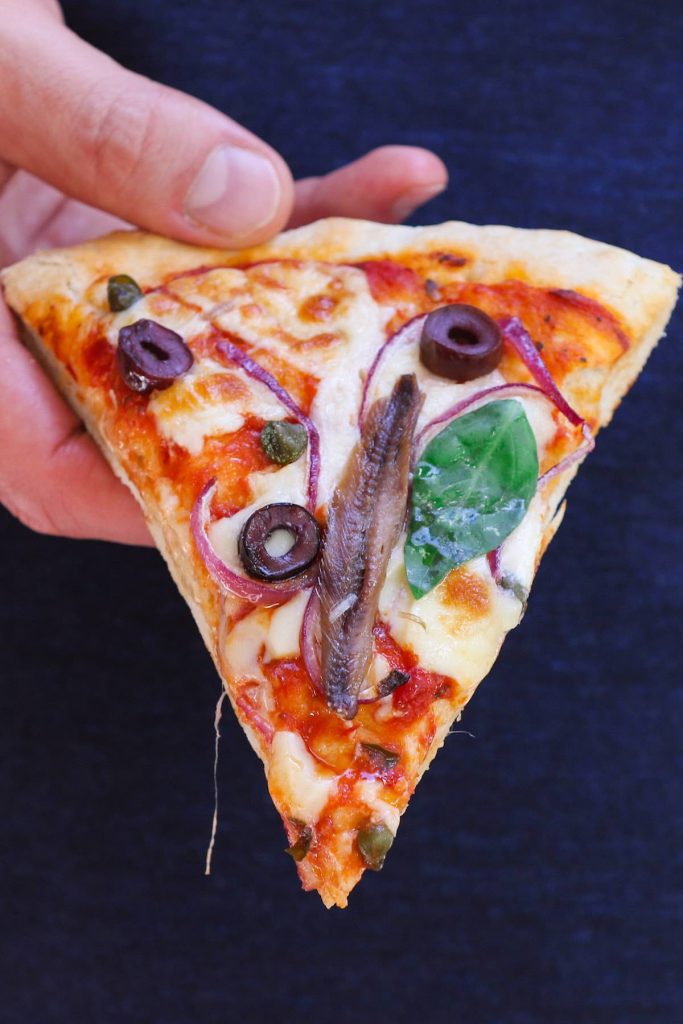 A slice of anchovy pizza fresh out of oven.