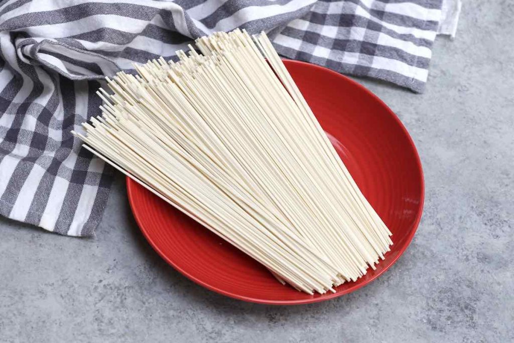 Uncooked Chinese dried noodles on a red plate.