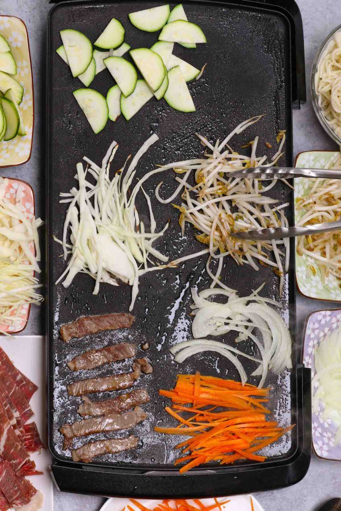 Cooking meat and vegetables on a hot griddle.