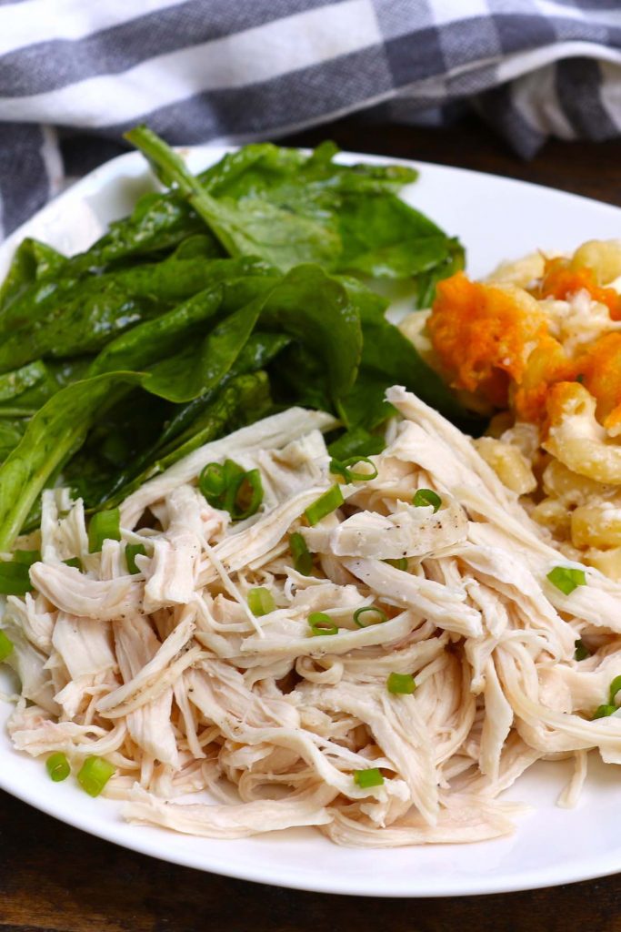 Sous vide cooked chicken breasts shredded and served with vegetables and pasta on a white plate.