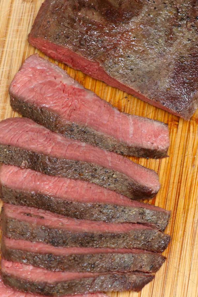Slicing cooked flat iron steak on a cutting board.