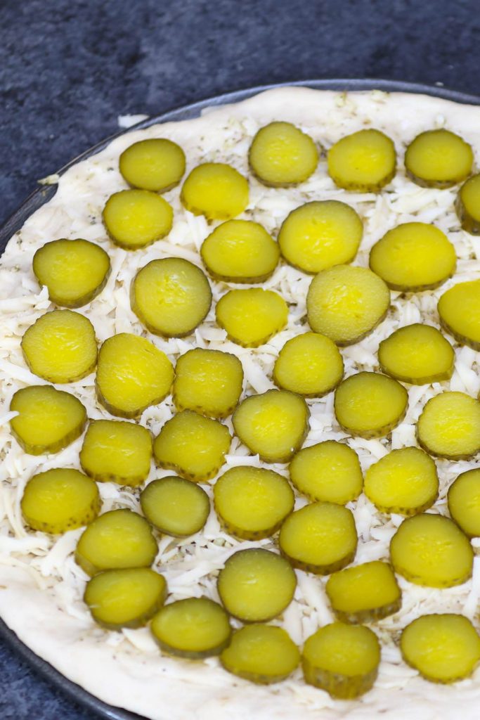 Adding toppings to garlic sauce brushed pizza crust.