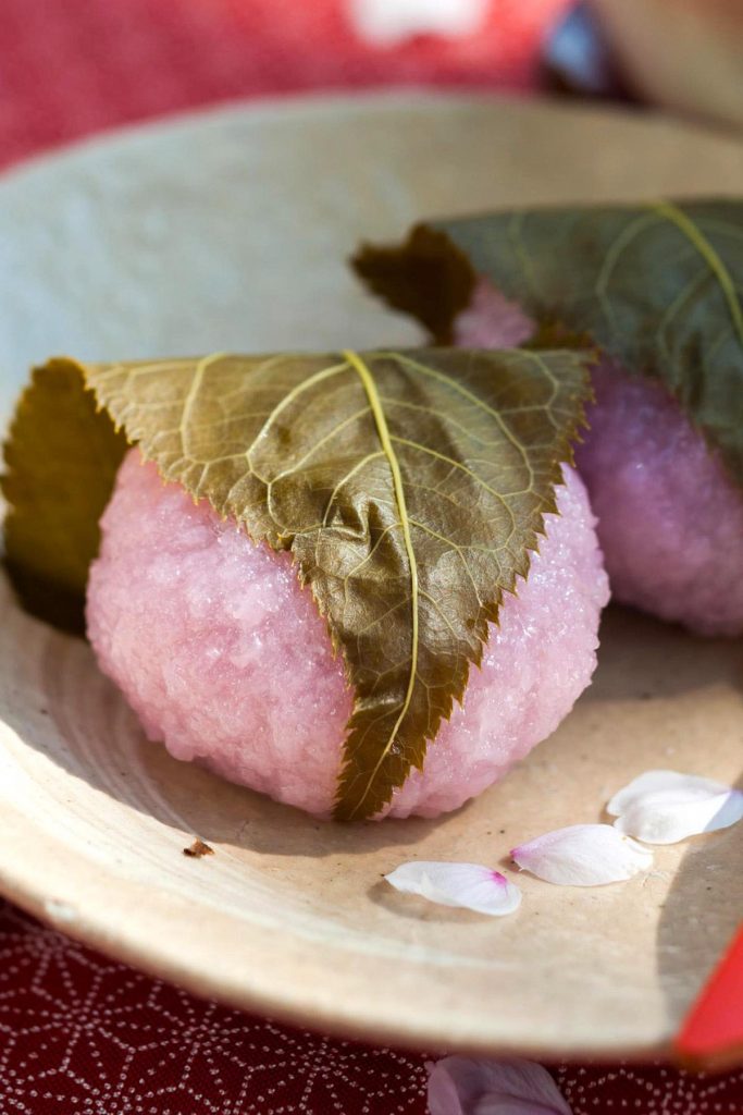 Easy Sakura Mochi with chewy and sticky rice cake on the outside, and sweet red bean paste filling on the inside! It’s rolled into beautiful pink mochi balls and covered with an edible pickled cherry blossom leaf. This Japanese dessert recipe is quick to make at home and perfect for celebrating the spring season or other special occasions. #SakuraMochi #PinkMochi