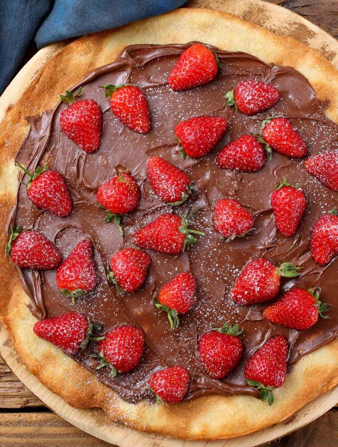 This Nutella Pizza is a must-try dessert that’s sure to impress your guest. It’s perfectly easy to make – this recipe skips out on the tomato and cheese in favor of adding chocolate spread onto the pizza crust, making a mouth-watering dessert. You can easily customize it with different topping ideas like strawberries, bananas, or marshmallows.
