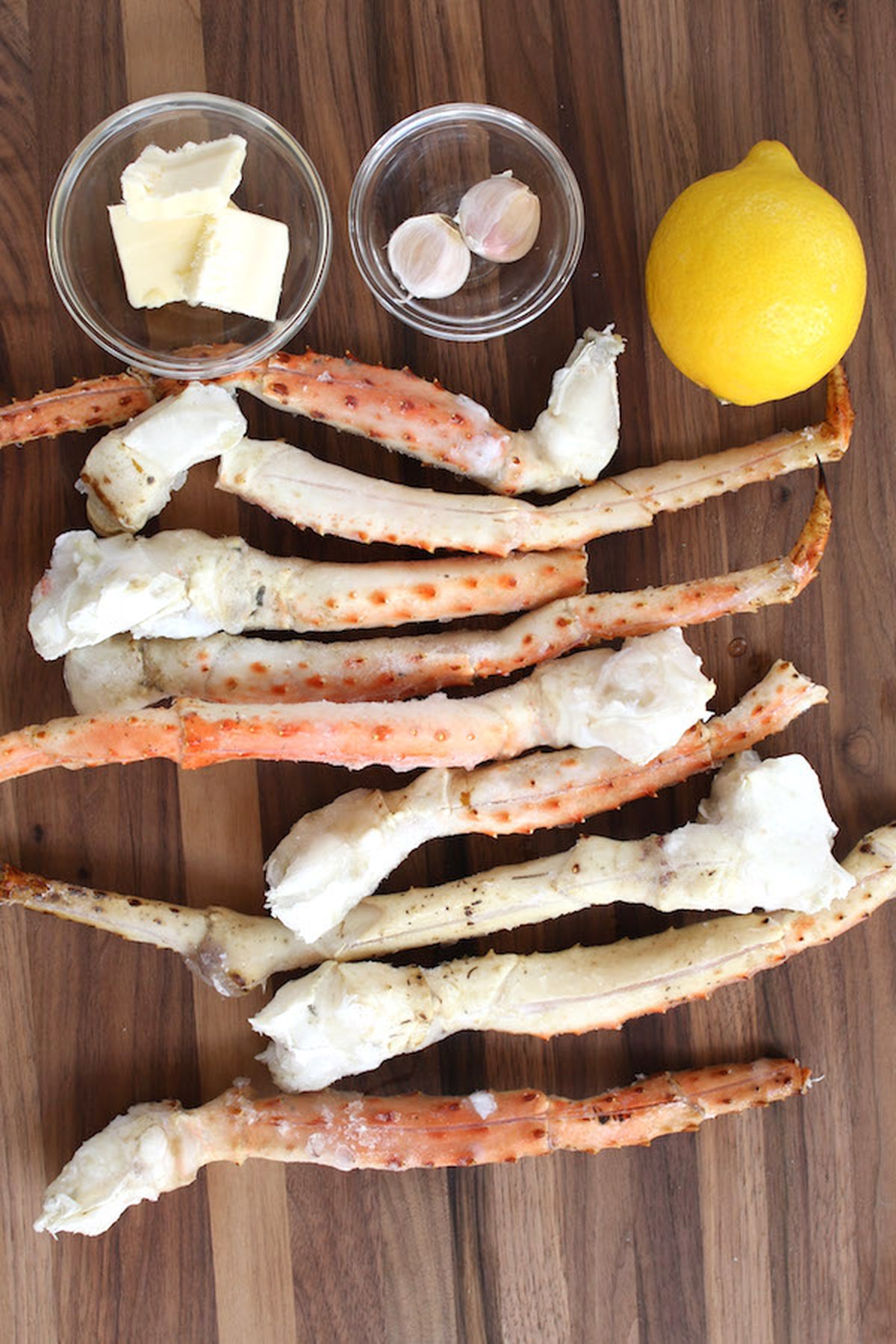 Crab legs, butter, garlic, and lemon on a wooden cutting board