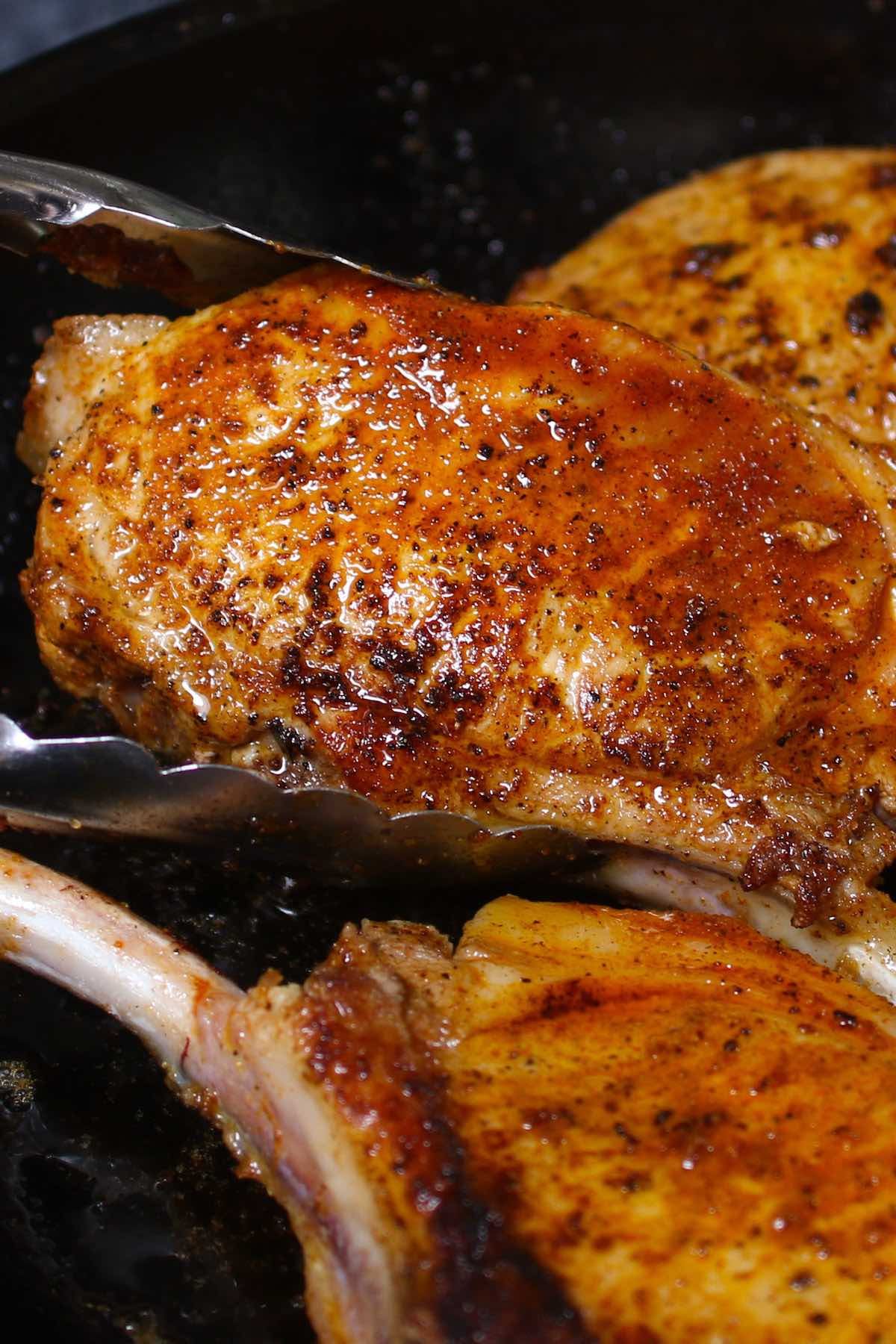 Golden brown baked pork ribeye chop with tongs on a baking sheet