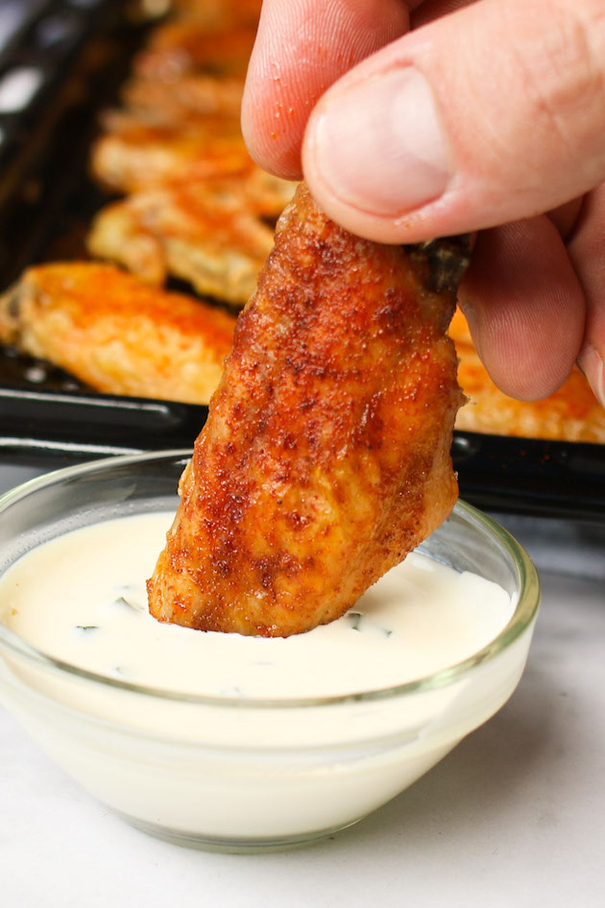 Crispy baked chicken wing being dipped into ranch dressing