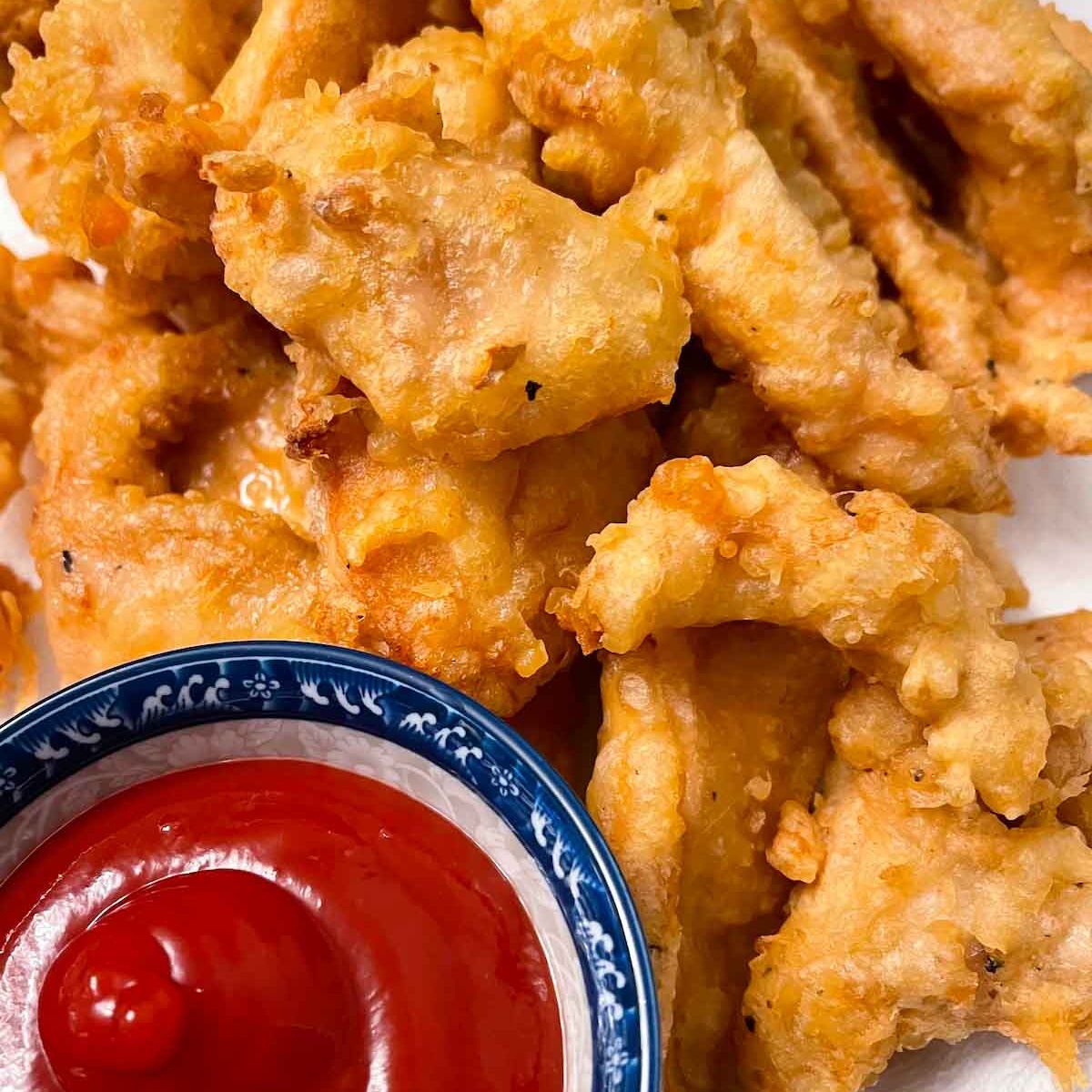 Close-up of crispy fried chicken pieces on a plate with a bowl of ketchup