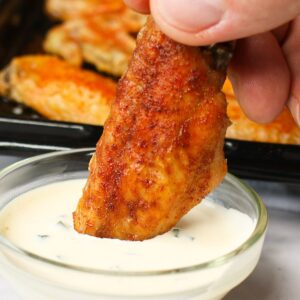 Crispy baked chicken wing being dipped into ranch dressing