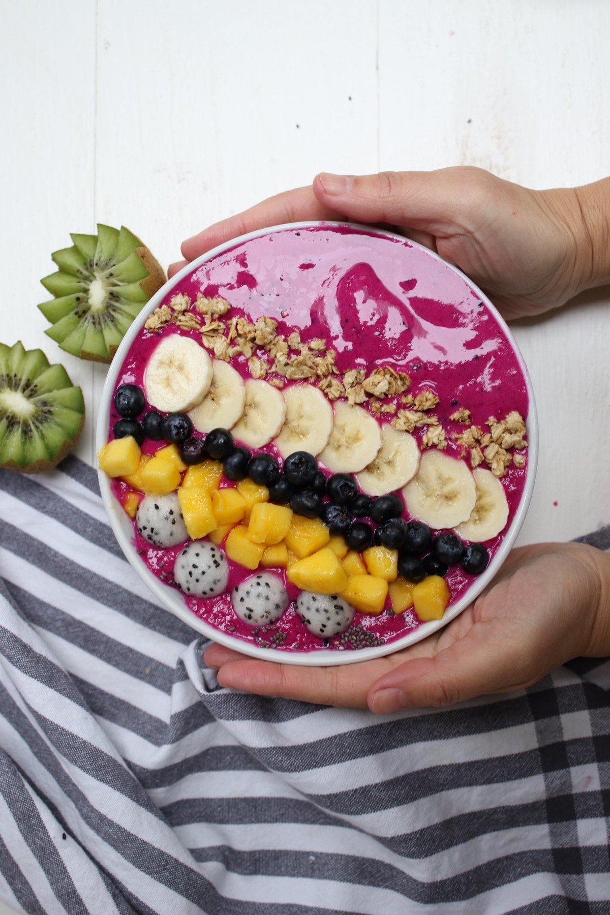 Tall glass of bright magenta dragon fruit smoothie with a pink straw and sliced white-fleshed dragon fruit resting on the rim