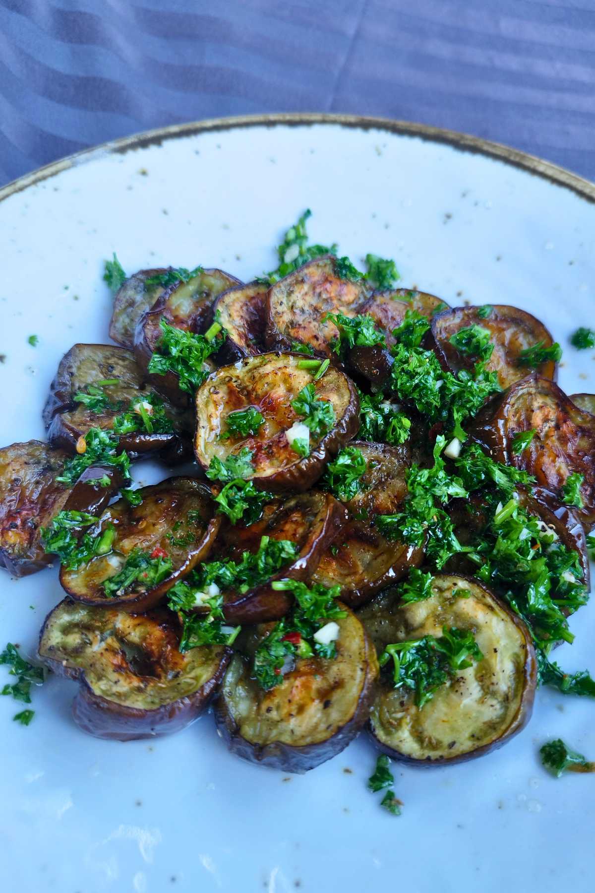 Roasted eggplant slices caramelized golden on the edges on a white plate with chimichurri sauce