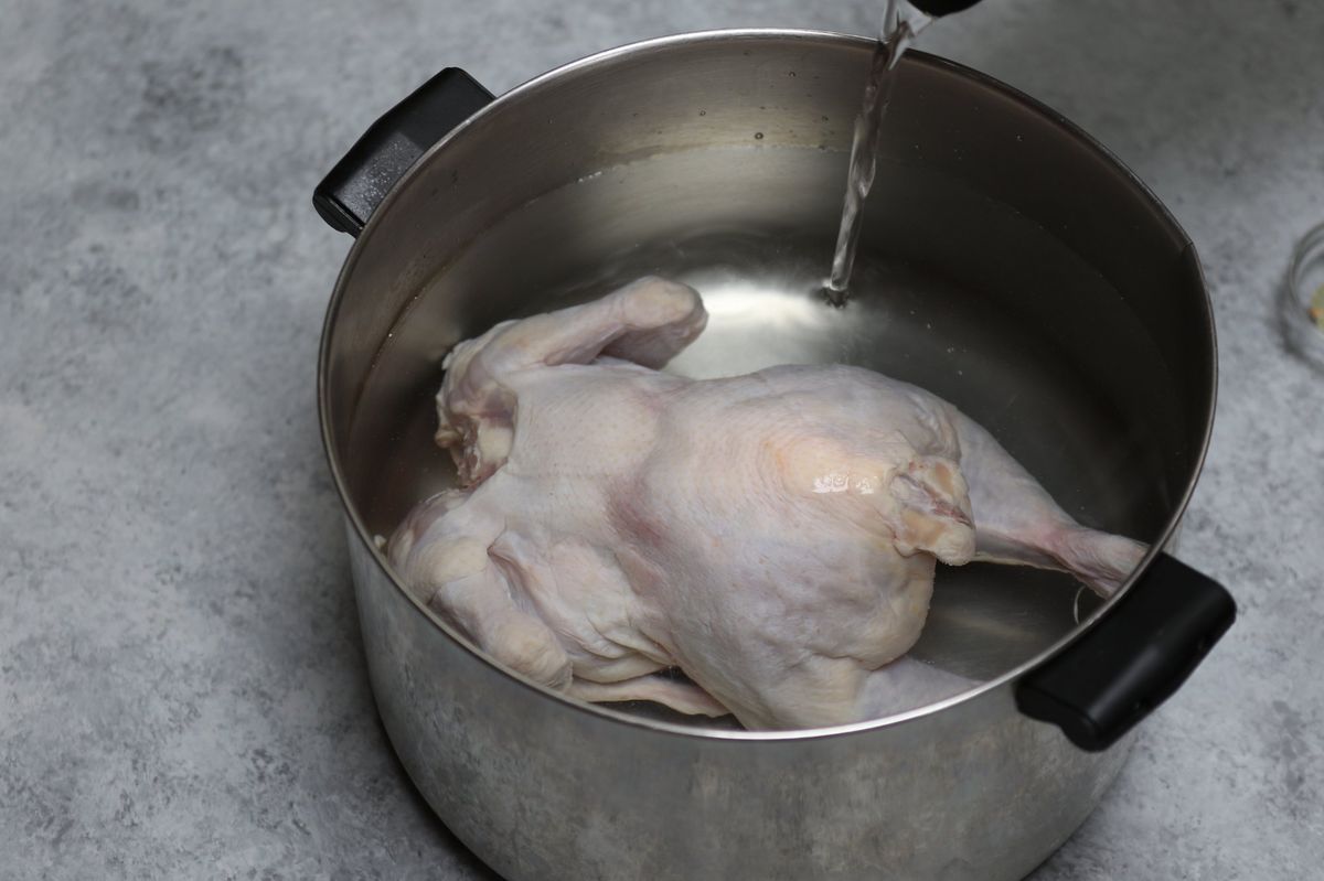 Raw whole chicken in a pot with water being poured in