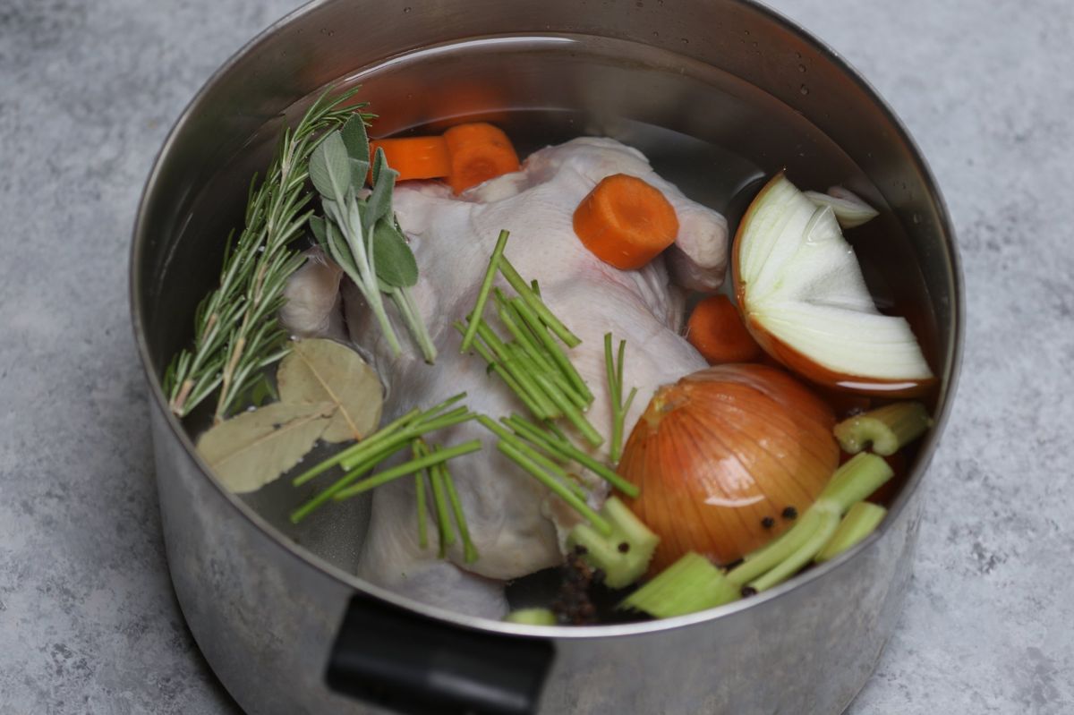 Raw chicken in a pot with carrots, onion, celery, rosemary, sage, and bay leaves before parboiling