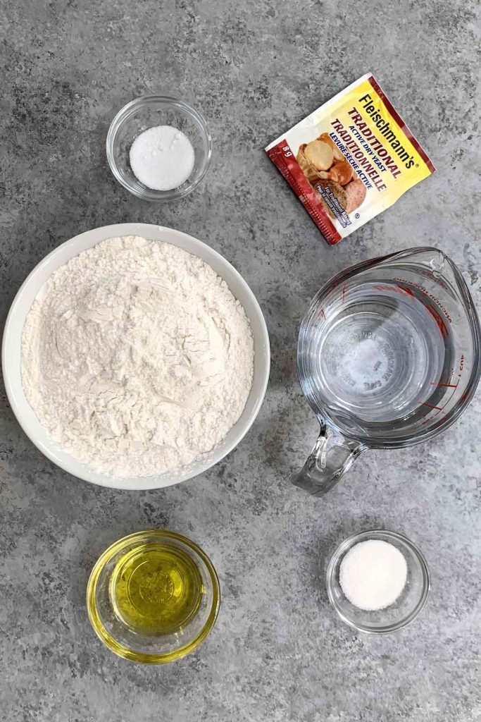 Pizza dough ingredients on the counter: yeast, all-purpose flour, warm water, olive oil, sugar, and salt