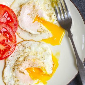 Breakfast recipes &ndash; two over medium eggs with runny yolks and sliced tomatoes on a plate with a fork