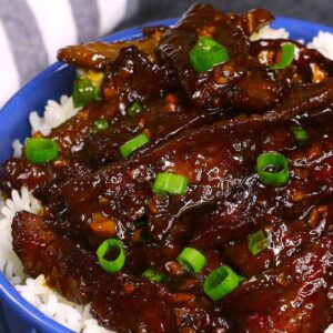 Chinese recipes &ndash; Mongolian beef stir fry with glossy brown sauce and green onions over steamed white rice in a blue bowl