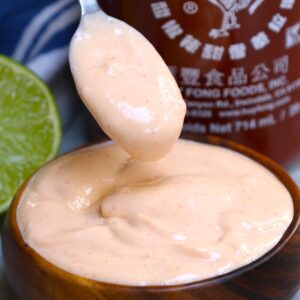 Sauce recipes &ndash; creamy onion ring dipping sauce on a spoon over a wooden bowl with Sriracha bottle and lime in the background