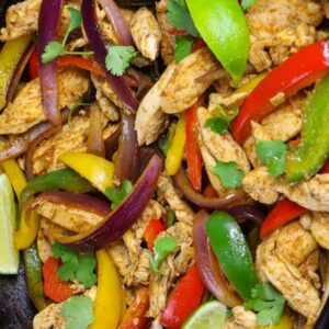 Slow cooker recipes &ndash; chicken fajitas with colorful bell peppers, red onions, cilantro, and lime wedges in a cast iron skillet