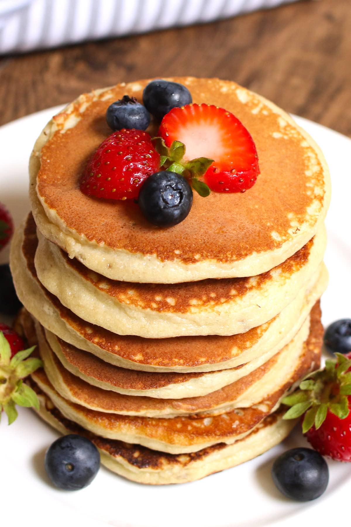 Pancakes stacked tall on a white plate, topped with fresh fruits