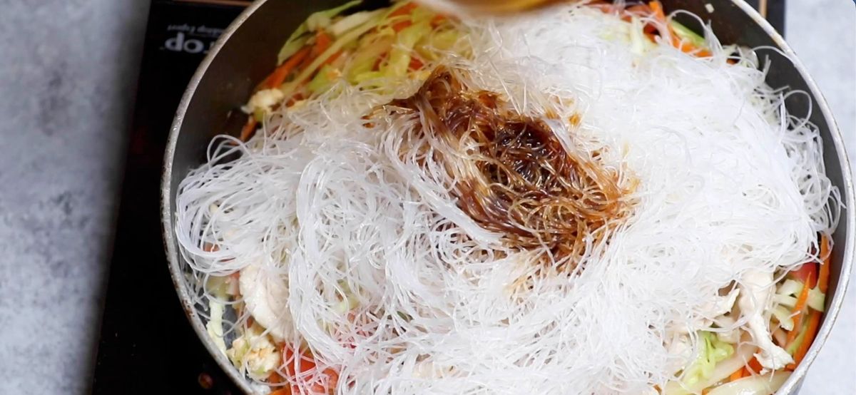 adding glass noodles to stir fry vegetables in a pan